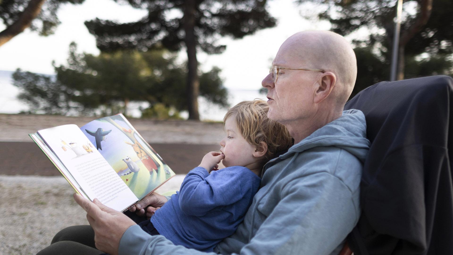 Ein Grossvater liest seinem Enkelkind ein Bilderbuch vor, 2022.