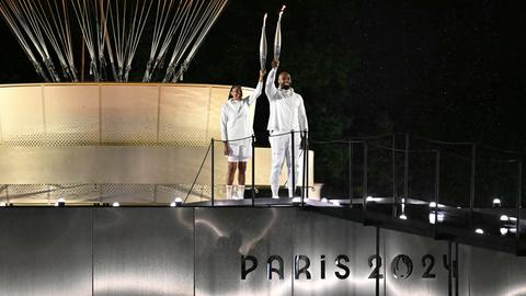 Eine Frau und ein Mann tragen die Olympische Fackel.