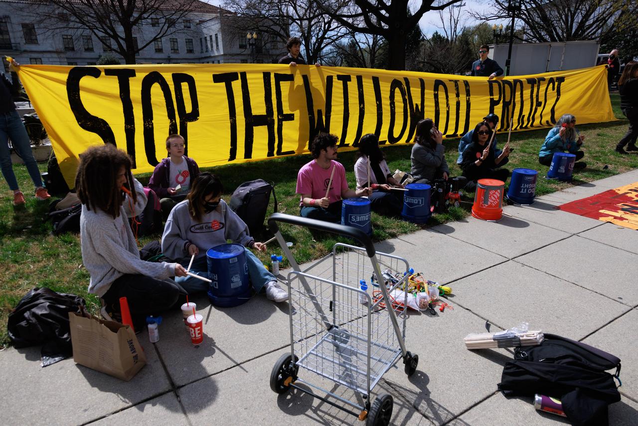 Menschen sitzen vor einem Banner mit der Aufschrift "Stop the Willow oil project".