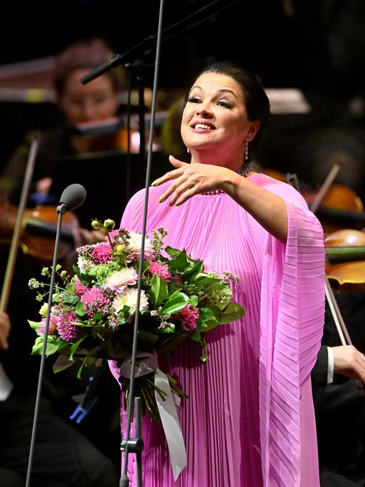 Anna Netrebko steht mit einem großen Blumenstrauß auf einer Bühne Anna Netrebko steht mit einem großen Blumenstrauß auf einer Bühne