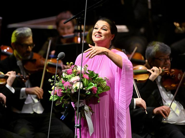 Anna Netrebko steht mit einem großen Blumenstrauß auf einer Bühne Anna Netrebko steht mit einem großen Blumenstrauß auf einer Bühne