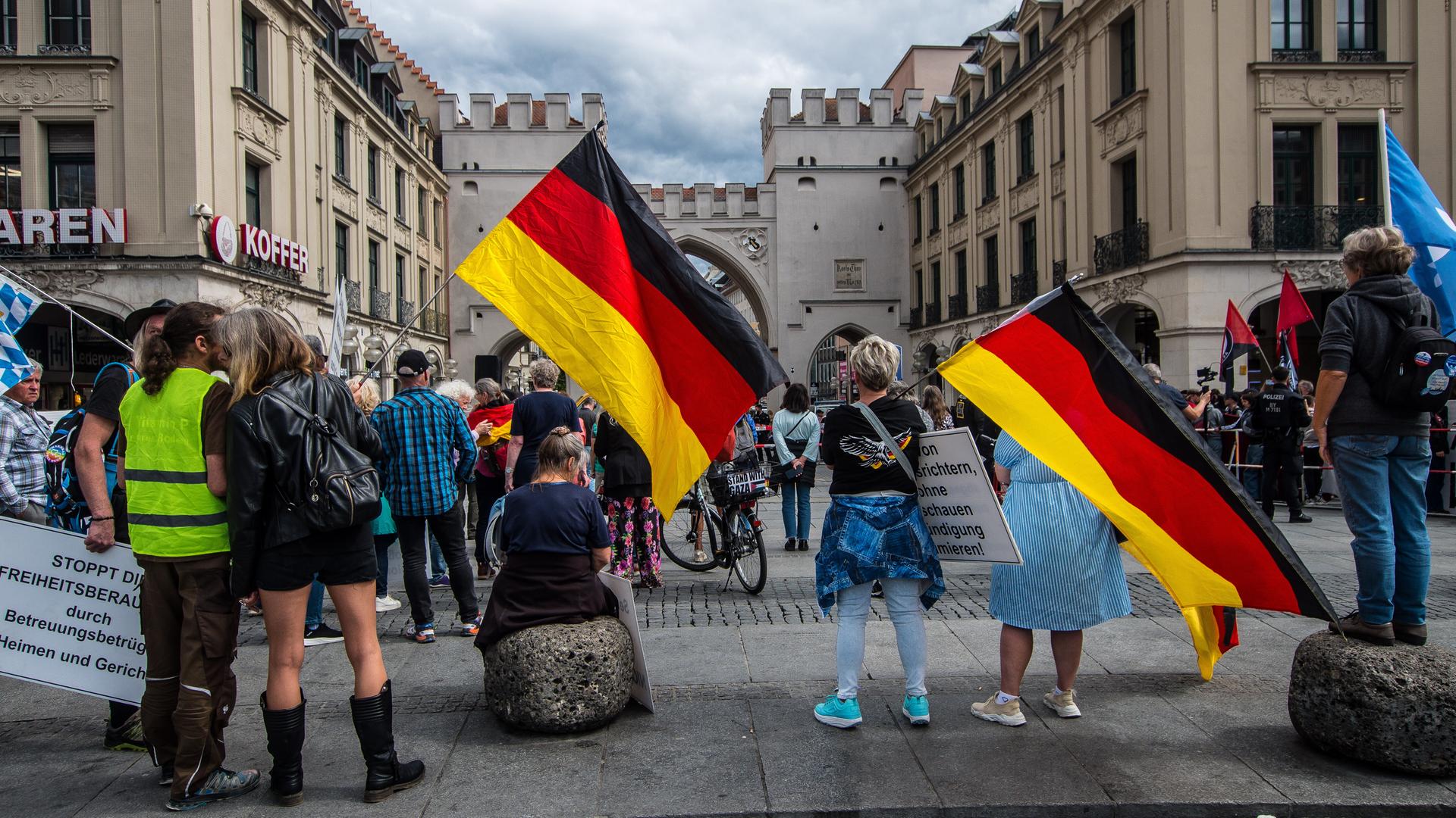Mehrere Menschen stehen auf einem Platz und halten Deutschlandfahnen in der Hand. Mehrere Menschen stehen auf einem Platz und halten Deutschlandfahnen in der Hand.