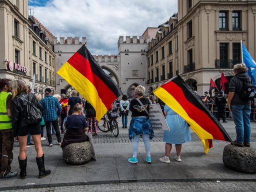 Mehrere Menschen stehen auf einem Platz und halten Deutschlandfahnen in der Hand.
