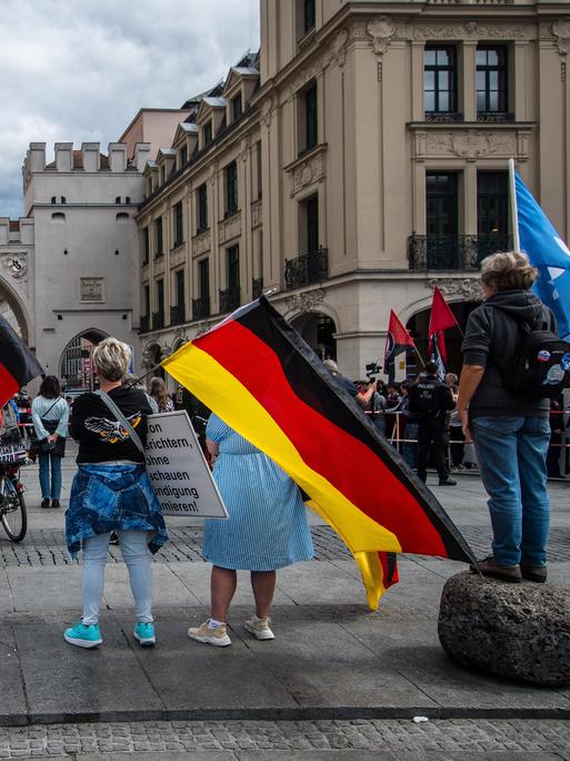 Mehrere Menschen stehen auf einem Platz und halten Deutschlandfahnen in der Hand. Mehrere Menschen stehen auf einem Platz und halten Deutschlandfahnen in der Hand.
