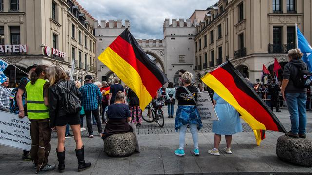 Mehrere Menschen stehen auf einem Platz und halten Deutschlandfahnen in der Hand.