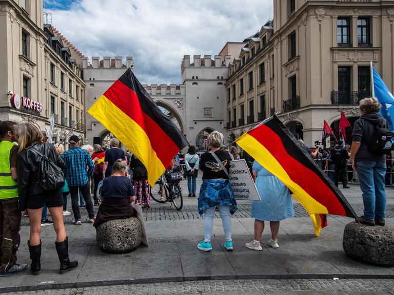 Mehrere Menschen stehen auf einem Platz und halten Deutschlandfahnen in der Hand. Mehrere Menschen stehen auf einem Platz und halten Deutschlandfahnen in der Hand.