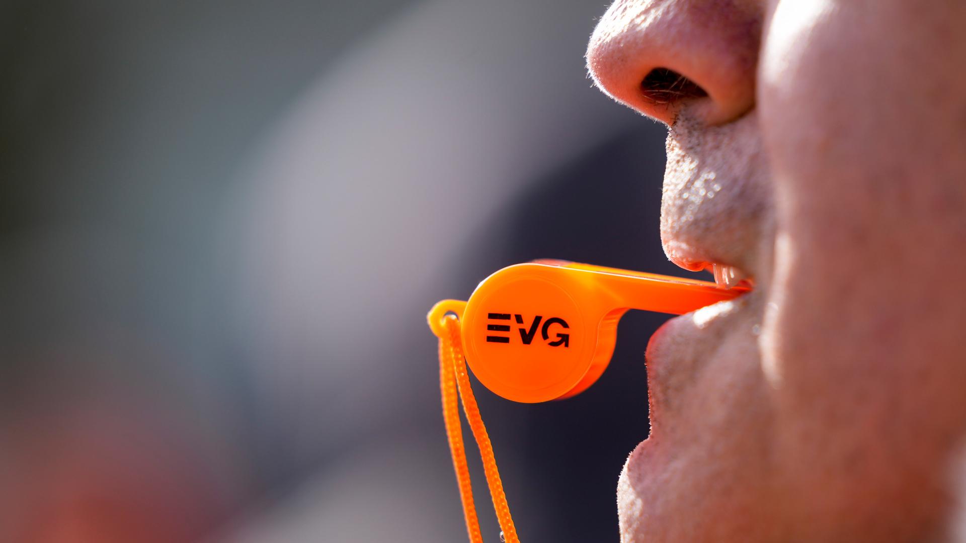 Eine neon-orange Trillerpfeife mit der Aufschrift EVG klemmt zwischen den Zähnen eines Mannes. Sein Gesicht ist nicht zu erkennen. Eine neon-orange Trillerpfeife mit der Aufschrift EVG klemmt zwischen den Zähnen eines Mannes. Sein Gesicht ist nicht zu erkennen.
