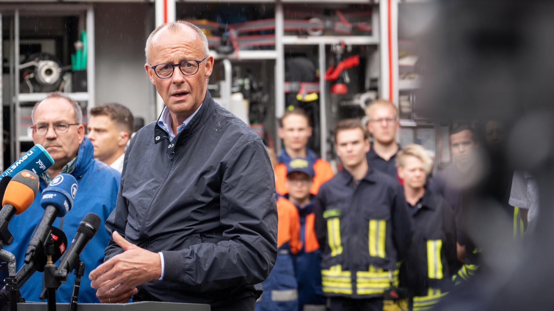 Merz spricht in mehrere Mikrofone. Hinter ihm sind der zuständige Landrat und mehrere Einsatzkräfte zu erkennen. Merz spricht in mehrere Mikrofone. Hinter ihm sind der zuständige Landrat und mehrere Einsatzkräfte zu erkennen.