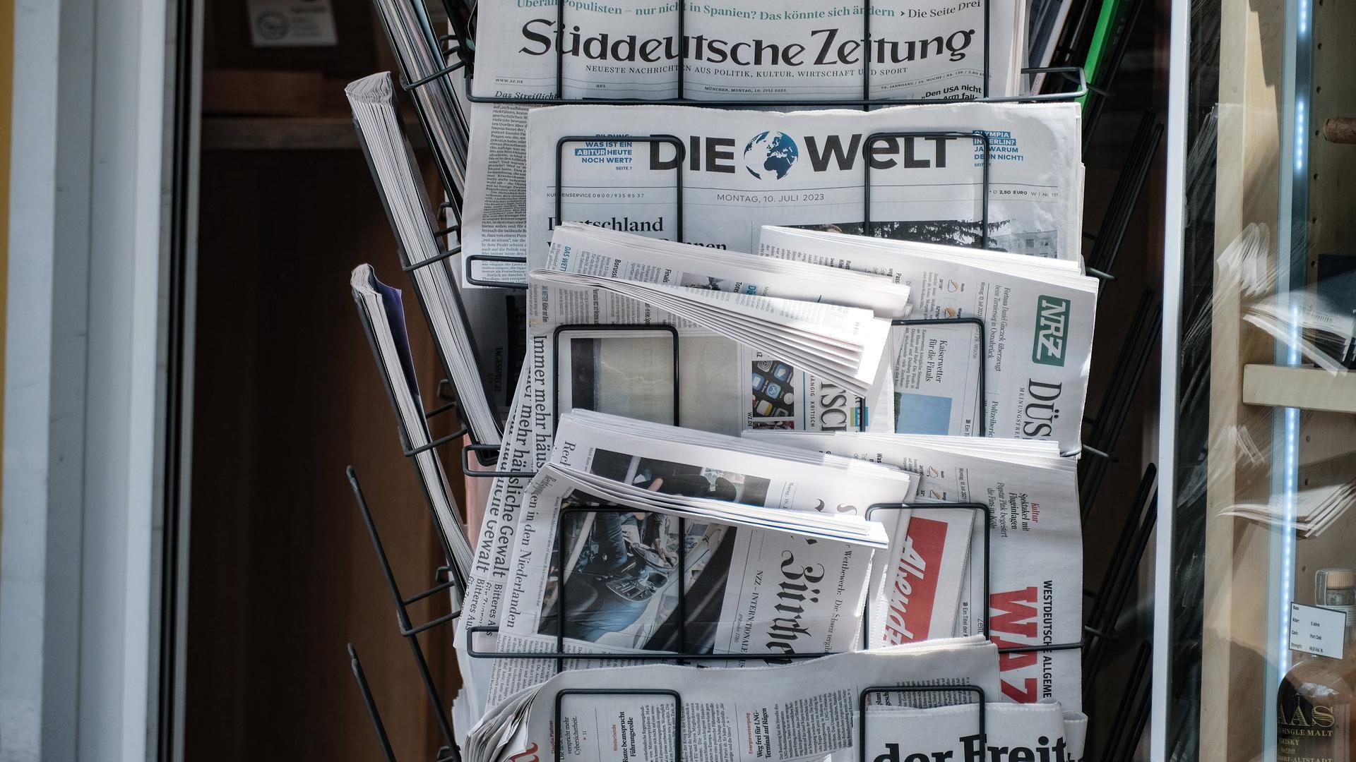 An einem Kiosk hängen nationale Zeitungen in einem Zeitungsständer. An einem Kiosk hängen nationale Zeitungen in einem Zeitungsständer.