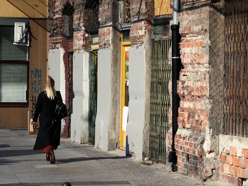 Warschauer Alltagsszene: Eine Frau geht auf dem Gehsteig an einem alten, unverputzten Mietshaus vorbei