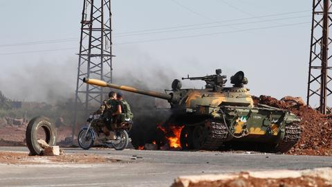 Syrische Regierungssoldaten fahren auf einem Motorrad an einem brennenden Panzer am Stadtrand von Sweida vorbei, wo es zu Zusammenstößen zwischen drusischen Milizen und sunnitischen Beduinenclans gekommen ist.