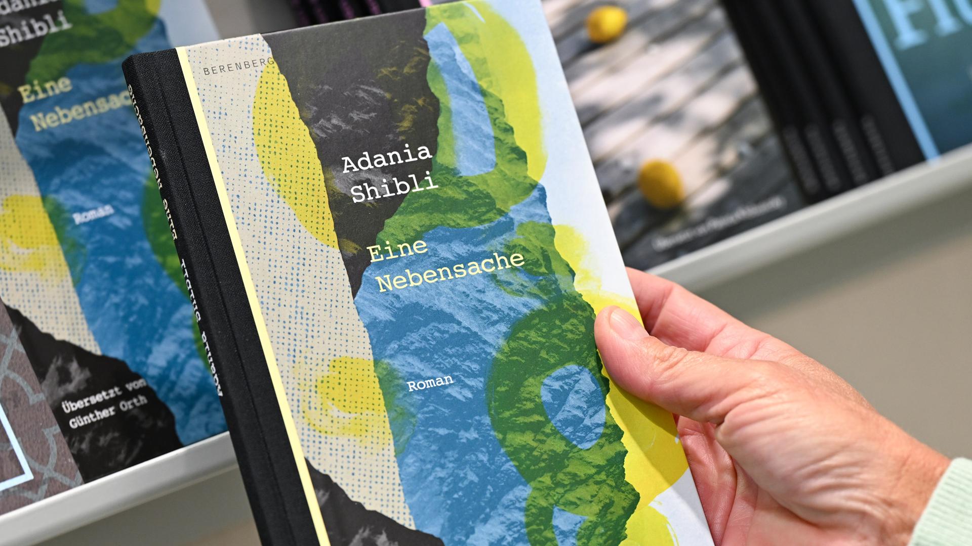 Eine Hand hält das Buch "Eine Nebensache" von Adania Shibli. Eine Hand hält das Buch "Eine Nebensache" von Adania Shibli.