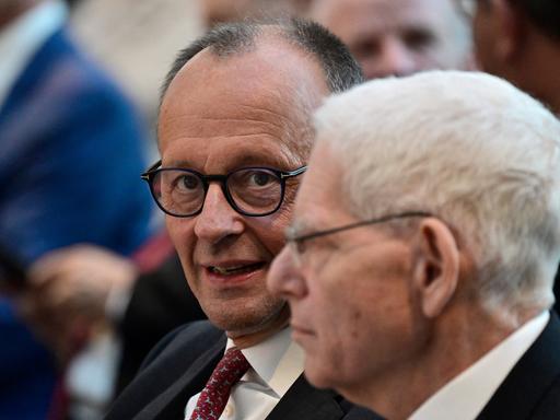 Bundeskanzler Friedrich Merz (CDU) und der Präsident des Zentralrats der Juden in Deutschland, Josef Schuster, sitzen nenbeneinander. Merz blickt in die Kamera, Schuster zum linken Bildrand. Er ist im Profil zu sehen.