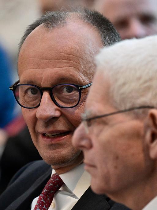 Bundeskanzler Friedrich Merz (CDU) und der Präsident des Zentralrats der Juden in Deutschland, Josef Schuster, sitzen nenbeneinander. Merz blickt in die Kamera, Schuster zum linken Bildrand. Er ist im Profil zu sehen.