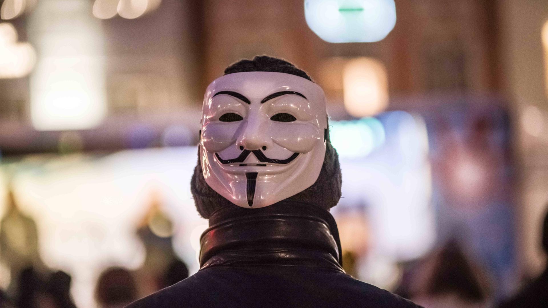 Ein Mann trägt auf dem Hinterkopf eine Maske des Anonymous.
