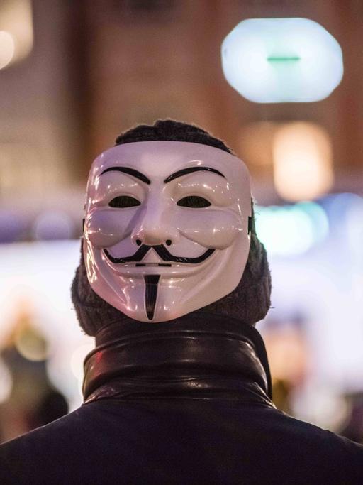 Ein Mann trägt auf dem Hinterkopf eine Maske des Anonymous.
