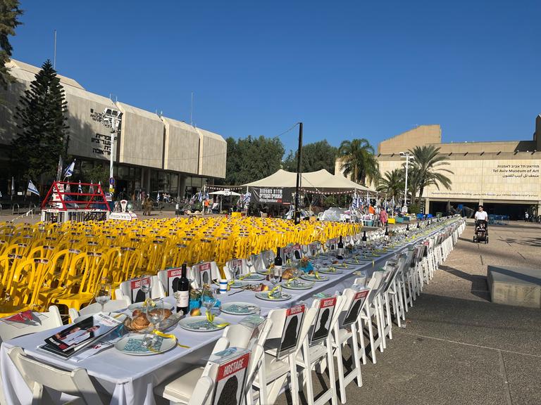 Auf dem Platz vor dem Kunstmuseum in Tel Aviv steht ein langer gedeckter Tisch für die Menschen, die seit dem Angriff der Hamas im israelischen Grenzgebiet als Geiseln gehalten und vermisst werden.