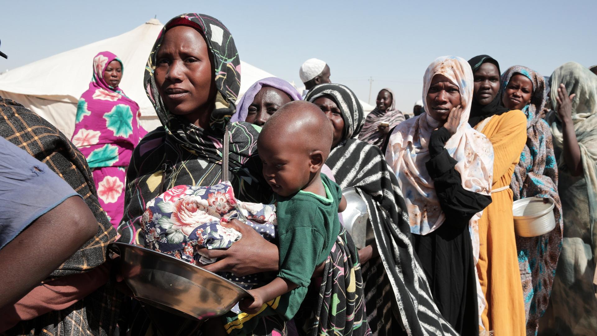 Das Foto zeigt Frauen und Kinder im Sudan. Sie sind auf der Flucht und stehen Schlange für Essen.