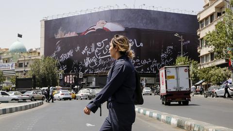 Eine unverhüllte Frau überquert den Revolutionsplatz in Teheran, über dem ein großes Billboard mit einem toten Donald Trump hängt.