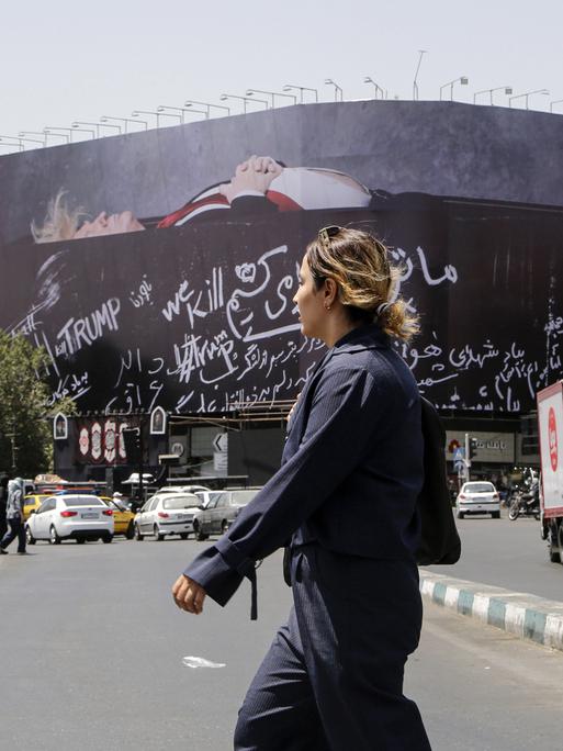 Eine unverhüllte Frau überquert den Revolutionsplatz in Teheran, über dem ein großes Billboard mit einem toten Donald Trump hängt.