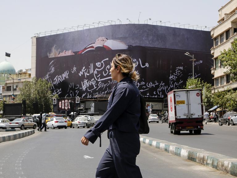 Eine unverhüllte Frau überquert den Revolutionsplatz in Teheran, über dem ein großes Billboard mit einem toten Donald Trump hängt.