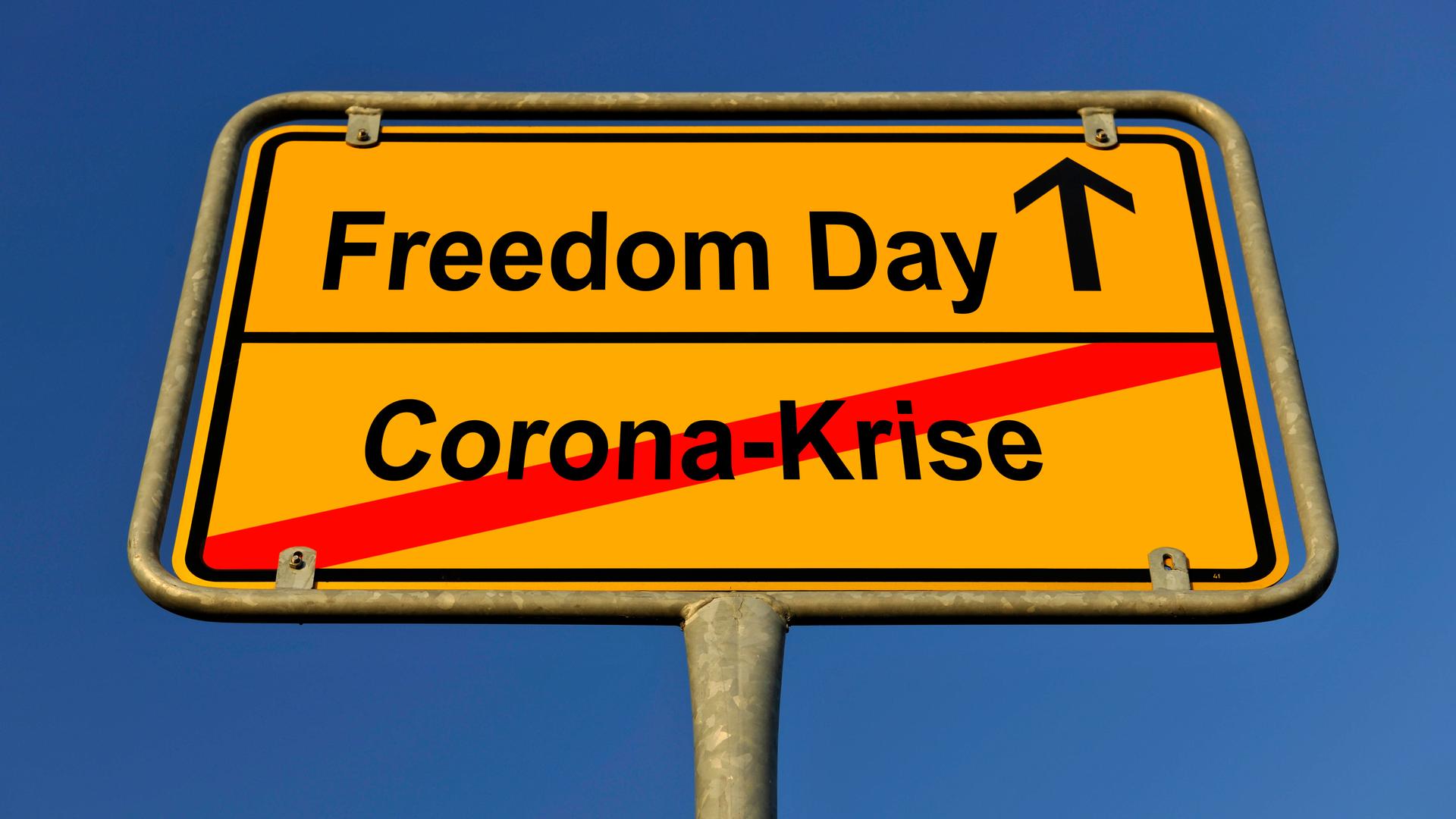 Ein Schild ist zu sehen, auf dem "Corona-Krise" durchgestrichen, darüber steht "Freedom Day".