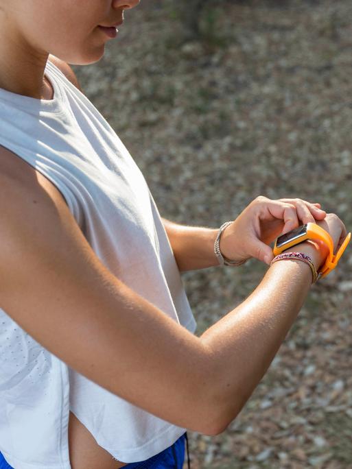 Eine junge Frau in Sportkleidung guckt auf iher Smartwatch.