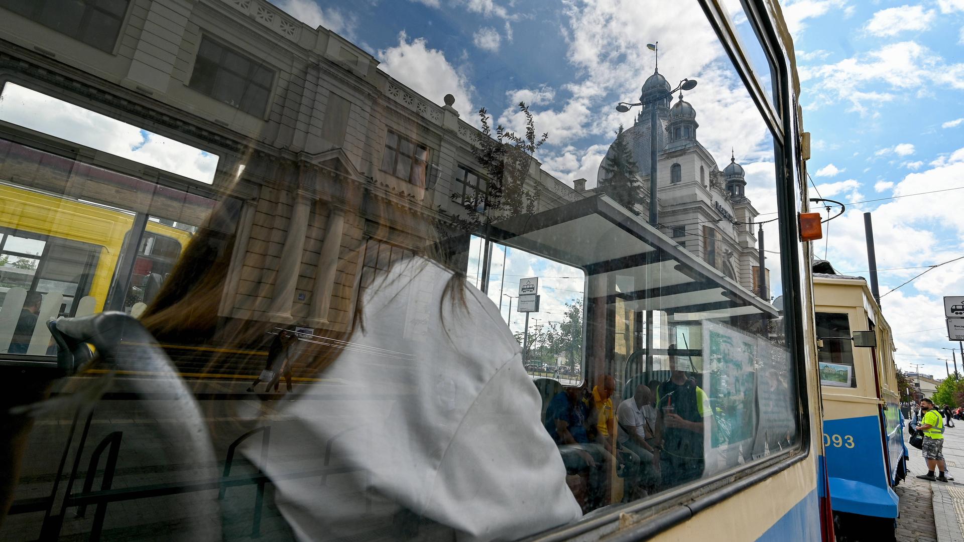 Eine Frau sitzt in einer historischen, blau-gelb gestrichenen Tram. Sie ist durch das Fenster nur von hinten zu sehen.