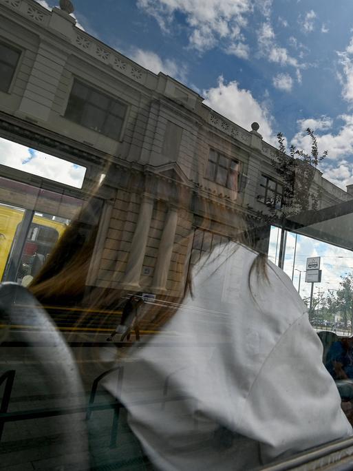 Eine Frau sitzt in einer historischen, blau-gelb gestrichenen Tram. Sie ist durch das Fenster nur von hinten zu sehen.