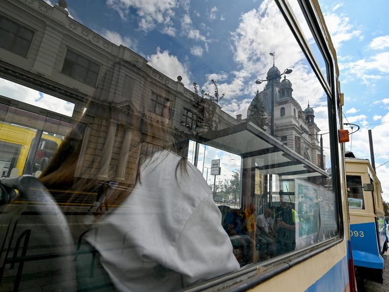 Eine Frau sitzt in einer historischen, blau-gelb gestrichenen Tram. Sie ist durch das Fenster nur von hinten zu sehen.