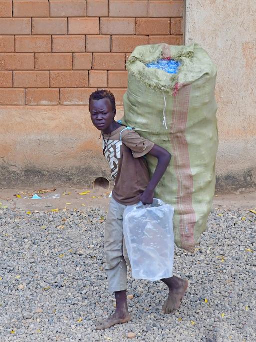 Ein Junge im Südsudan trägt eingesammelte Plastikflaschen in Taschen zu einer Annahmestelle, wo das Plastik wiederverwertet wird, und er für seine Sammlung einen geringen Geldbetrag erhält, aufgenommen am 13.06.2021. 