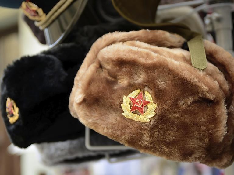 Traditionelle russische Wintermützen, die mit sowjetischen Abzeichen verziert sind, werden in einem Souvenirladen zum Verkauf angeboten.