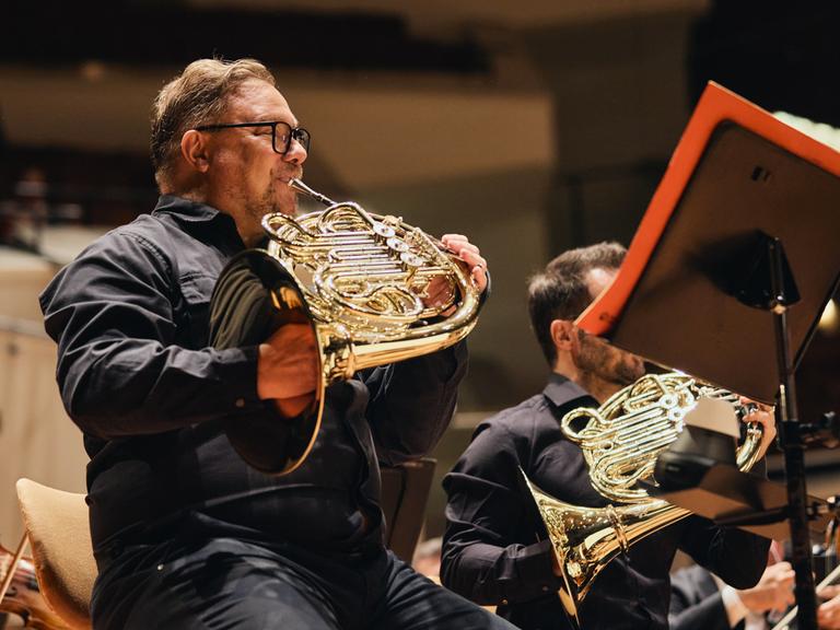 Blick auf einen Hornisten mit Instrument, der in einer Reihe mit seinen Kollegen sitzt und spielt.