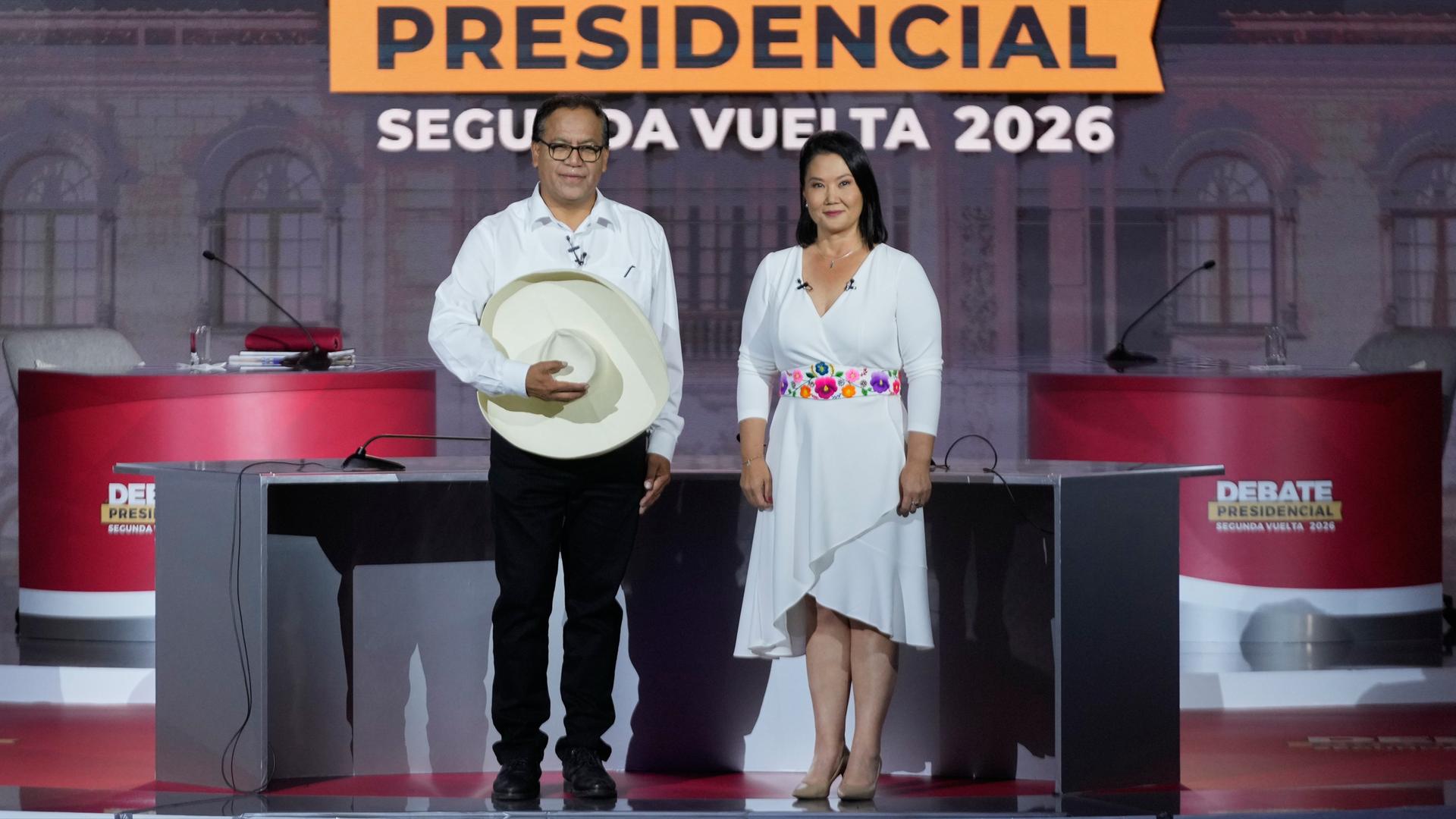 Die Präsidentschaftskandidaten Keiko Fujimori (rechts) und Roberto Sánchez (rechts) stehen auf einer Bühne. Sie trägt ein weißes Kleid, er ein weißes Hemd und eine schwarze Hose. Vor dem Bauch hält Roberto Sánchez einen traditionell peruanischen Hut.