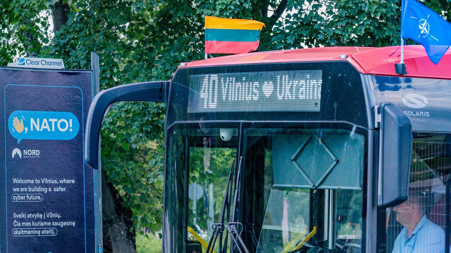 Vorbereitungen des NATO-Gipfels in den Straßen von Vilnius. Zu sehen ist ein Bus mit den Flaggen der Nato und Litauens. Auf der Anzeige des Busses steht "Vilnius loves Ukraine". 