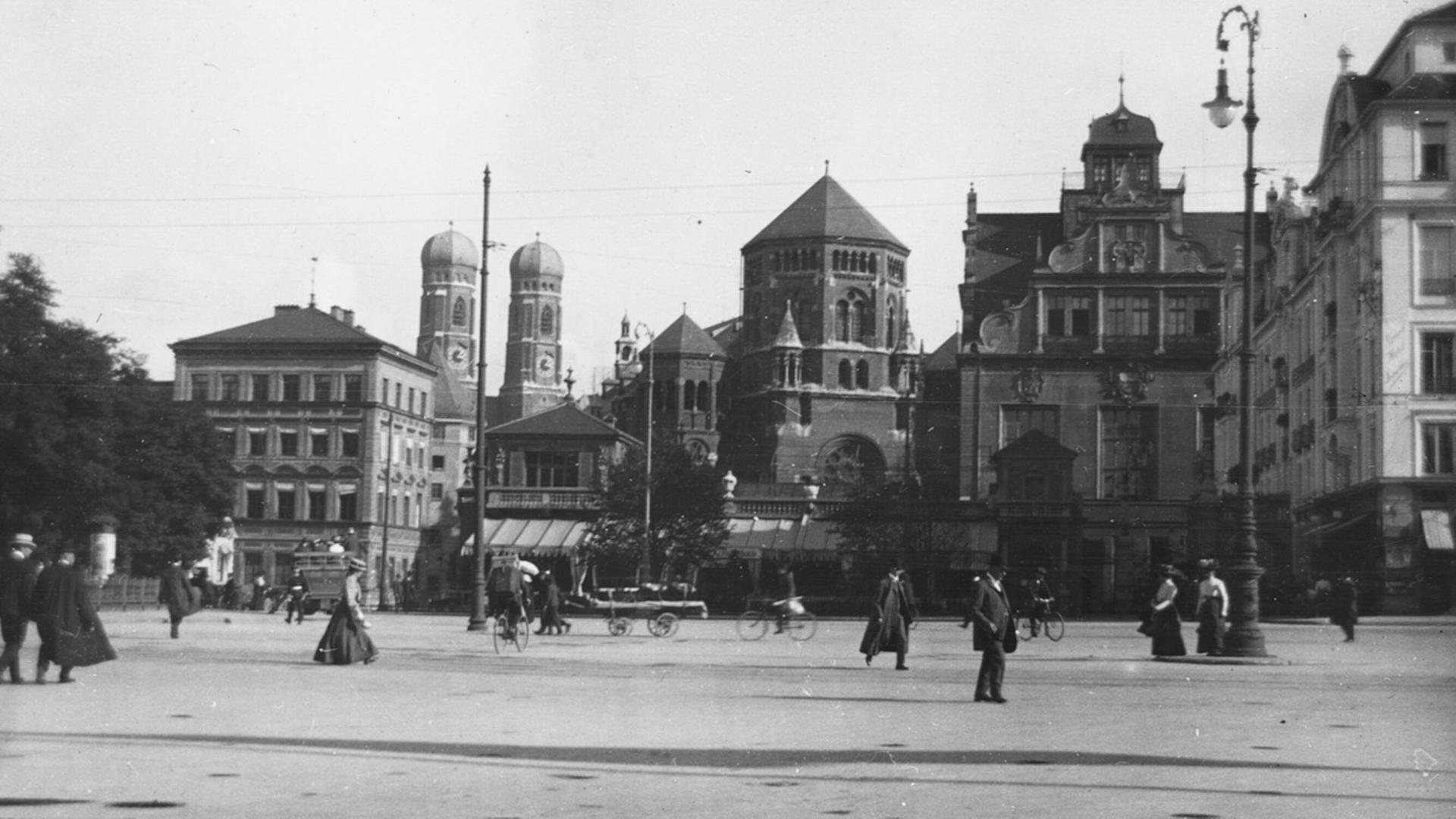 Schwarz-weiß Straßenaufnahme der Westenrierstraße in München mit der damaligen Hautsynagoge Anfang des vergangenen Jahrhunderts. Im Hintergrund die Stadt und die Synagoge, im Vordergrund gehen Menschen vorbei. Schwarz-weiß Straßenaufnahme der Westenrierstraße in München mit der damaligen Hautsynagoge Anfang des vergangenen Jahrhunderts. Im Hintergrund die Stadt und die Synagoge, im Vordergrund gehen Menschen vorbei.