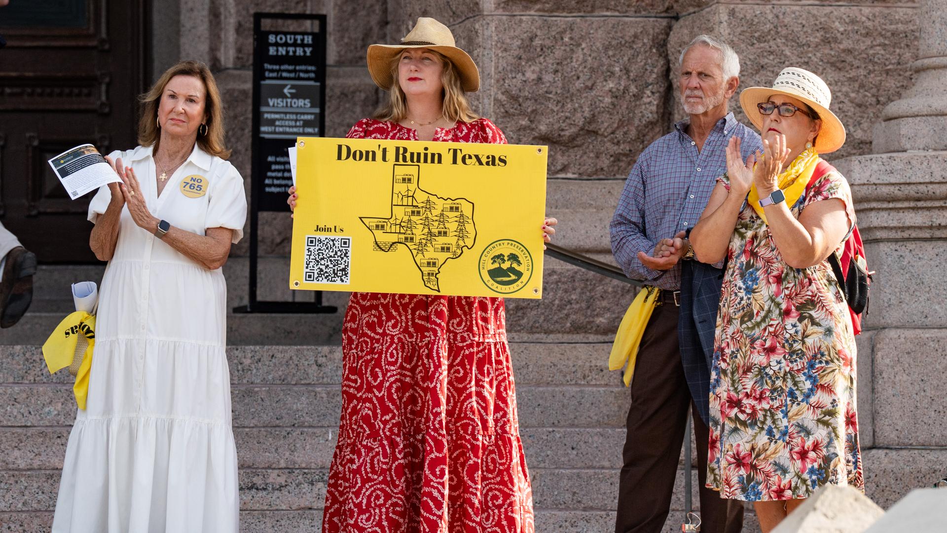Vier Personen stehen bei einer Demonstration auf einer Straße. Eine Frau in rotem Kleid hält ein gelbes Schild in die Luft, auf dem "Don't ruin Texas" steht. Vier Personen stehen bei einer Demonstration auf einer Straße. Eine Frau in rotem Kleid hält ein gelbes Schild in die Luft, auf dem "Don't ruin Texas" steht.