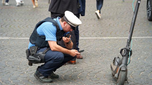 Ein Polizist kontrolliert einen E-Scooter. Er hat ein Handy in der Hand und überprüft die Daten.   