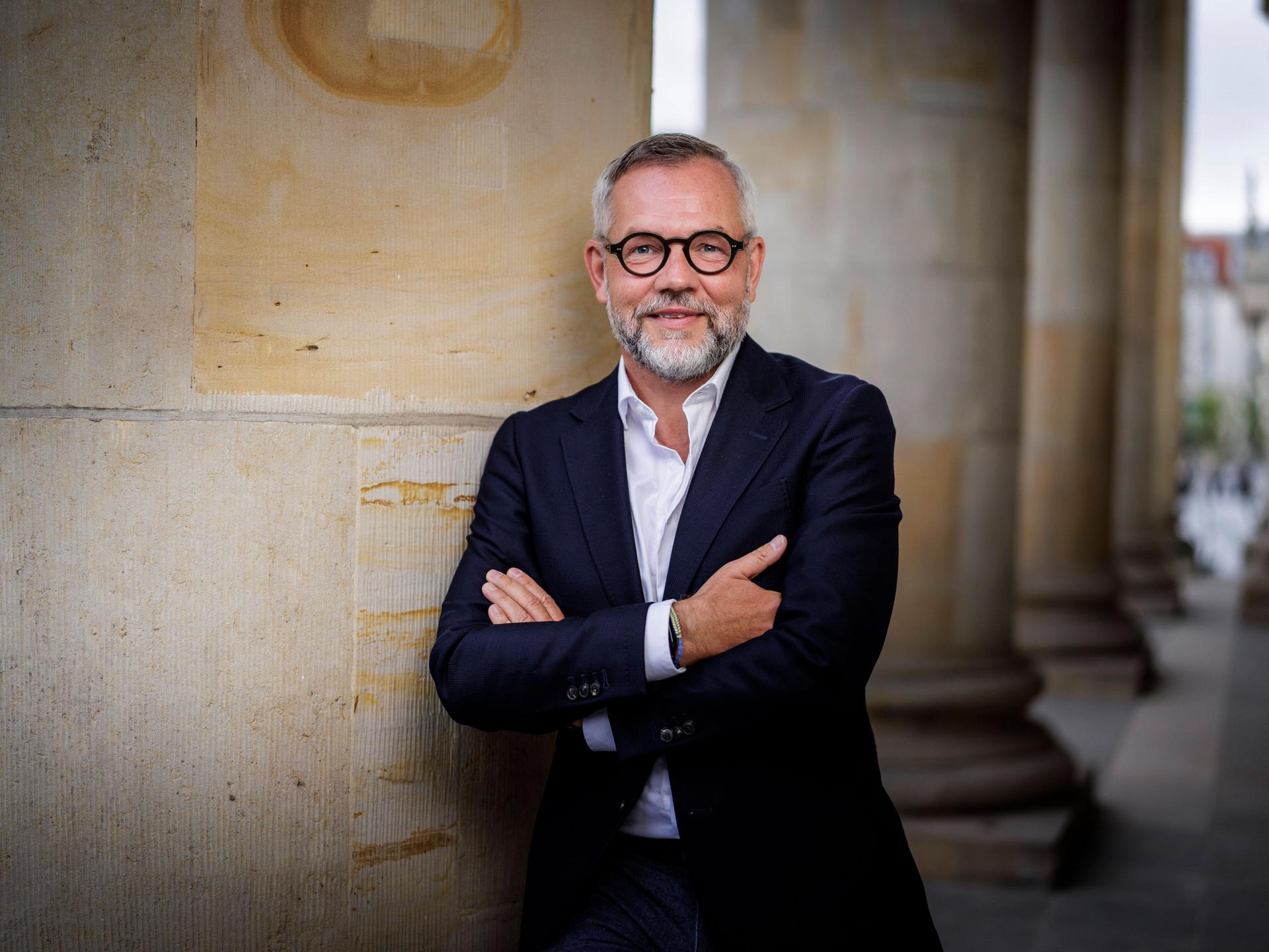 Michael Roth lehnt in lockerer Pose an einer großen Säule und lächelt in die Kamera.