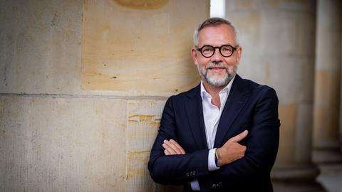 Michael Roth lehnt in lockerer Pose an einer großen Säule und lächelt in die Kamera.