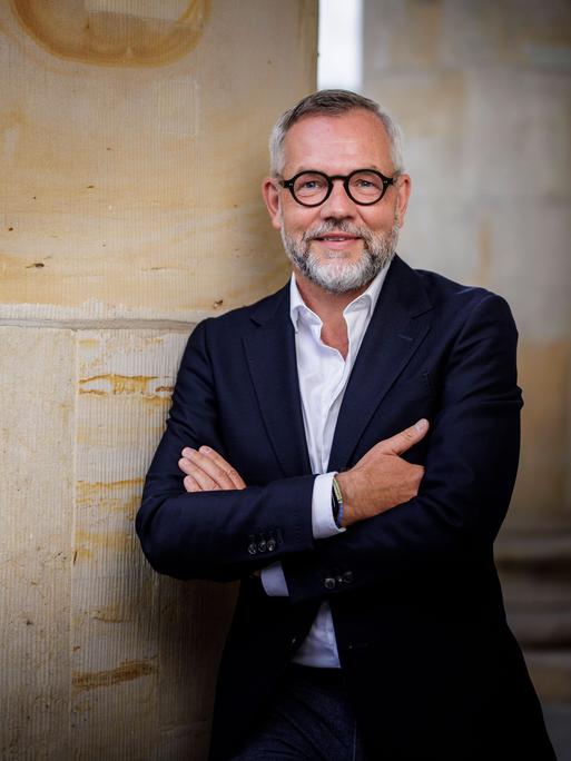 Michael Roth lehnt in lockerer Pose an einer großen Säule und lächelt in die Kamera.