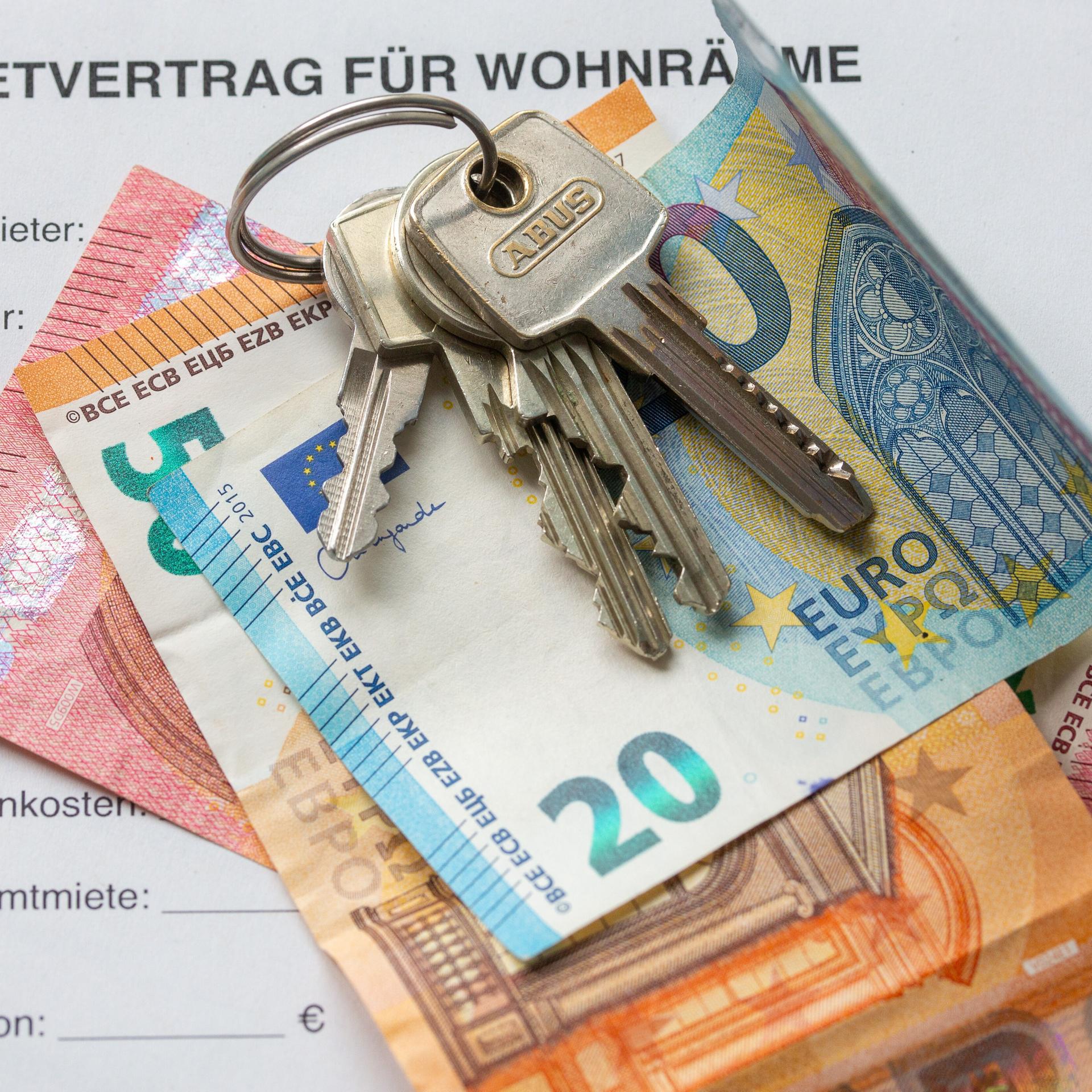 Ein Mietvertrag liegt zusammen mit Geldscheinen und Wohnungsschlüsseln auf einem Tisch.
