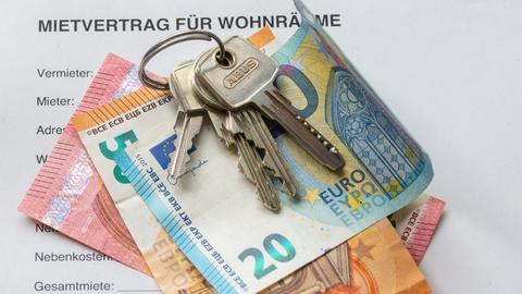 Ein Mietvertrag liegt zusammen mit Geldscheinen und Wohnungsschlüsseln auf einem Tisch.