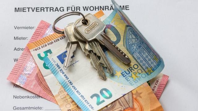 Ein Mietvertrag liegt mit Geldscheinen und Wohnungs-Schlüsseln auf einem Tisch.