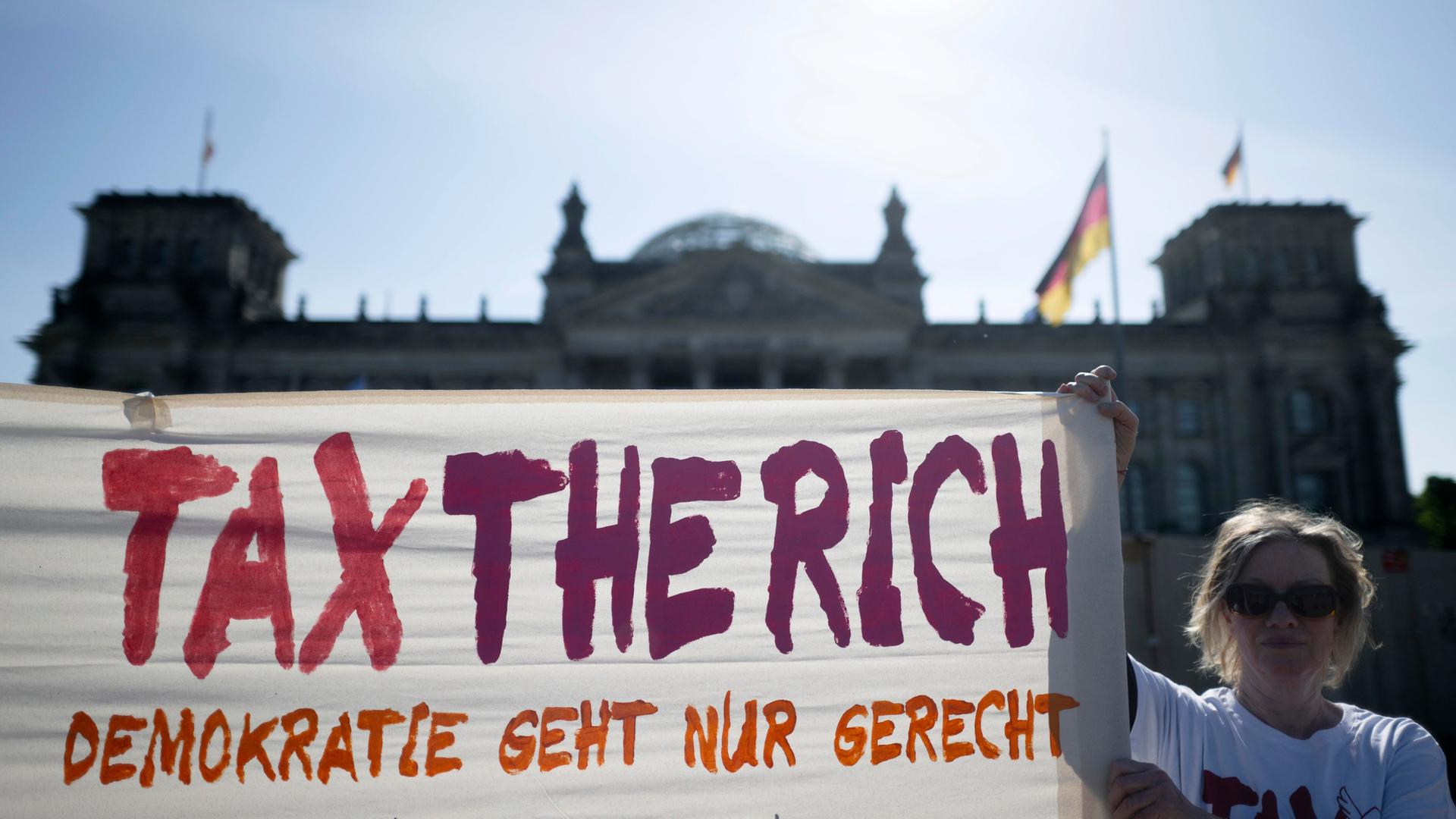 Eine Frau hält ein Transparent mit der Aufschrift "Tax the rich - Demokratie geht nur gerecht" vor dem Deutschen Bundestag hoch