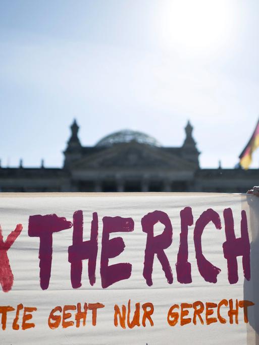 Eine Frau hält ein Transparent mit der Aufschrift "Tax the rich - Demokratie geht nur gerecht" vor dem Deutschen Bundestag hoch