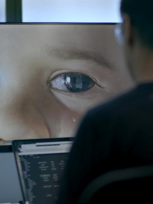 Im Still aus "Eternal You" sitzt eine Person an einem Computer, auf dem die Großaufnahme des Auges eines Babies zu sehen ist.