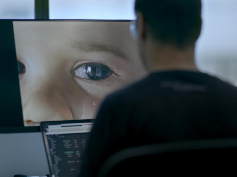 Im Still aus "Eternal You" sitzt eine Person an einem Computer, auf dem die Großaufnahme des Auges eines Babies zu sehen ist.