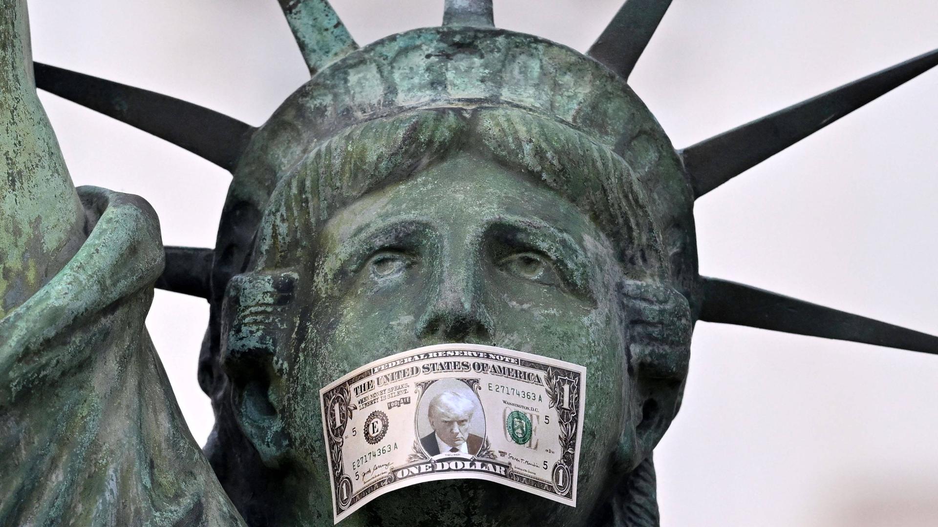 Nachbildung der Freiheitsstatue mit einer Dollarnote als Knebel, die Donald Trumps Porträt zeigt. (Aktion des Künstlers Toolate in Nizza)