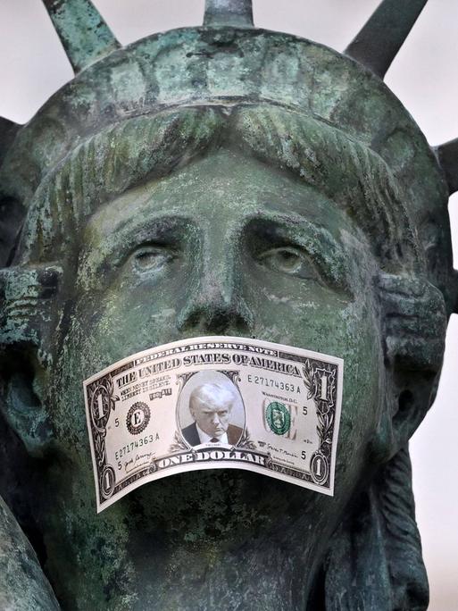 Nachbildung der Freiheitsstatue mit einer Dollarnote als Knebel, die Donald Trumps Porträt zeigt. (Aktion des Künstlers Toolate in Nizza)